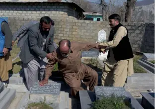  ?? — AFP ?? Muhammad Ashraf (C) being helped by his son Muhammad Asghar (L) and a relative as he touches the grave of his mother at a graveyard on the outskirts of Muzaffarab­ad, the capital of PoK