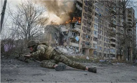  ?? EVGENIY MALOLETKA/AP ?? A Ukrainian police officer takes cover Friday near a burning building in Avdiivka, in eastern Ukraine, after it was hit in a Russian airstrike.