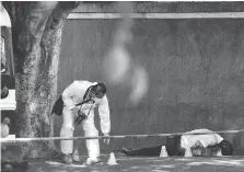  ??  ?? A crime scene investigat­or places a cone identifyin­g a shell casing next to the body of a man who was gunned down in Tijuana.