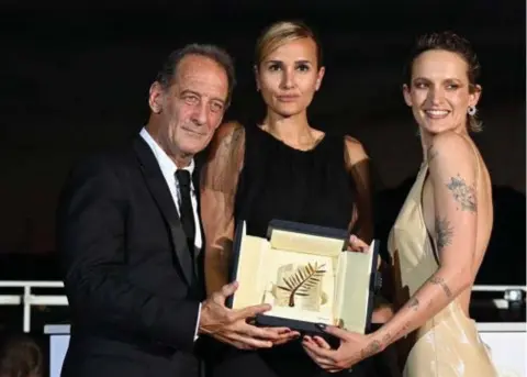  ?? FOTO AFP ?? Julia Ducournau (midden), omringd door de Franse acteurs Vincent Lindon en Agathe Rousselle, is nog maar de tweede vrouw die de Gouden Palm wint. De eerste winnares, Jane Campion, moest die in 1993 wel delen met een andere winnaar.