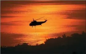  ?? MIKE ELIASON/SANTA BARBARA COUNTY FIRE DEPARTMENT VIA AP ?? In this photo provided by the Santa Barbara County Fire Department, with Montecito, Calif. and the Pacific Ocean in the distance, a helicopter hovers over a reservoir to fill a bucket with water as the fight against a wildfire continues Tuesday, Dec....