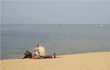  ?? ASSOCIATED PRESS ?? South Lake Tahoe resident Connor Jones sits with his dog on a smoke-cloaked empty beach in South Lake Tahoe, Calif., Monday Sept. 6, 2021. Residents who fled South Lake Tahoe under threat of a wildfire were allowed to return as crews stalled the flames from advancing.