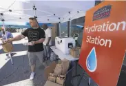  ?? Ted S. Warren / Associated Press ?? Carlos 0amos hands out bottles of water and sack lunches at a hydration station in Seattle.