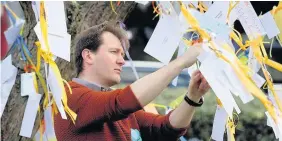  ??  ?? > Richard Ratcliffe ties messages of support to a tree in Fortune Green, West Hampstead, London, yesterday