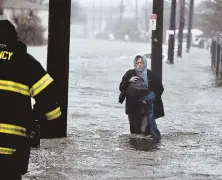  ??  ?? CUT OFF: A woman, left, wades through knee-deep water while evacuating from Houghs Neck in Quincy, during widespread flooding yesterday, right.