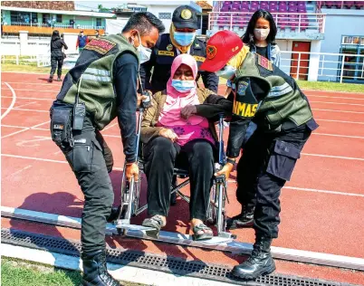  ?? DIPTA WAHYU/JAWA POS ?? KAMI BANTU, BU: Petugas satpol PP membantu seorang warga berkursi roda yang mendatangi Lapangan THOR untuk menjalani vaksinasi.