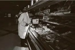  ?? LM Otero / Associated Press ?? Raul Alonzo uses the light from a cellphone to arrange products at a grocery in Dallas. Some power retailers, like Griddy, are urging customers to leave.