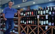  ??  ?? Frank Gonzalez, owner of the two locations of Frank's Fish & Seafood Market, shows some of the wine selections available at the store in Columbus.