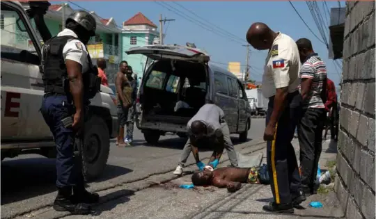  ?? ?? EDS NOTE: GRAPHIC CONTENT - Police and a forensic attend to the body of a person lying in the street in the Delmas area of Port-au-prince