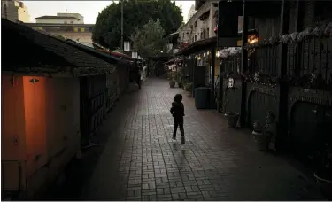  ?? JAE C. HONG — THE ASSOCIATED PRESS ?? A lone boy plays on an empty Olvera Street in downtown Los Angeles earlier this month. The tree-covered brick alley typically teeming with tourists is empty. Many of the shops that sell everything from traditiona­l Mexican folk dresses to paintings of artist Frida Kahlo to sombreros are padlocked and the ones open have few, if any, customers.