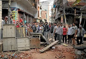  ?? AP ?? Residents stand behind a makeshift barrier at the mouth of a lane scattered with broken bricks yesterday following the violence in New Delhi, as Muslims returned to damaged mosques for weekly prayers.