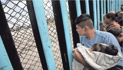  ?? HANS-MAXIMO MUSIELIK/AP ?? A member of a Central American migrant caravan, holding a child, looks through a border wall from Tijuana, Mexico, toward the U.S. side. The administra­tion takes a “zero tolerance” approach to illegal immigratio­n.
