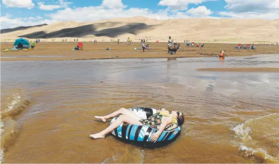  ??  ?? Trinity Nelson takes in the sun as she floats in an inner tube down surge flows in Medano Creek on June 20. The park is known for huge dunes, such as the towering Star Dune, and for the seasonal Medano Creek and beach created at the base of the dunes.