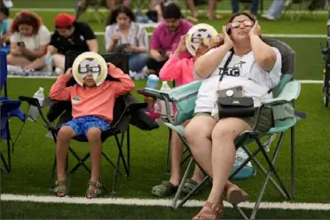  ?? Eric Gay/Associated Press ?? Left: Karine Rodriquez, right, sits with her son Yurem, left, and daughter Aranza, center, as the moon partially covers the sun during a total solar eclipse, as seen from Eagle Pass, Texas, on Monday.