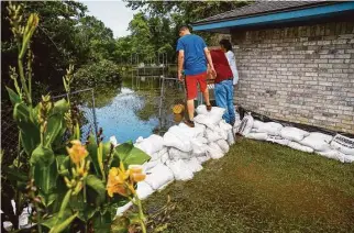  ??  ?? Volunteers check out the rising floodwater­s being held back by sandbags. So far, the dams have been holding and have limited damages to minor flooding in a few homes.