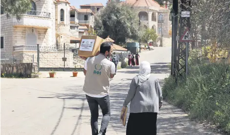  ??  ?? A volunteer from the Humanitari­an Aid Foundation (İHH) carries an aid package delivered to an elderly woman, in Beirut, Lebanon, May 7, 2021.