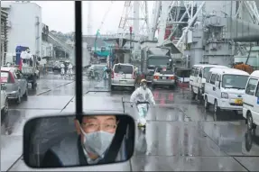  ?? TOMOHIRO OHSUMI / REUTERS ?? A worker in a protective suit and a mask is seen through a bus window at Tokyo Electric Power Co’s Fukushima Daiichi nuclear power plant in Fukushima, Japan, on Thursday.