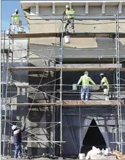  ??  ?? Constructi­on workers haul plaster to the top of a scaffold.