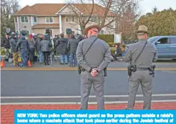  ?? — AFP ?? NEW YORK: Two police officers stand guard as the press gathers outside a rabbi’s home where a machete attack that took place earlier during the Jewish festival of Hanukkah, in Monsey, New York, yesterday.