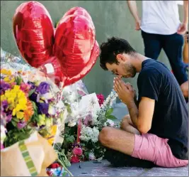  ?? ASSOCIATED PRESS ?? PAOLO SINGER, 27, A SILVER LAKE RESIDENT, prays at a makeshift memorial of flowers, candles and notes growing on the sidewalk outside the Silver Lake Trader Joe’s store in Los Angeles Monday.