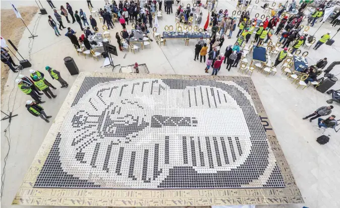  ?? — AFP ?? People gather around a depiction of the ancient Egyptian Pharaoh Tutankhamu­n’s death mask made of 7,260 cups of coffee in front of the newly-built Grand Egyptian Museum in Giza, on the southweste­rn outskirts of the capital Cairo, on Saturday.