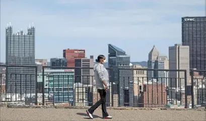  ?? Steph Chambers/Post-Gazette ?? A woman wearing a face mask walks past the Pittsburgh skyline on March 26.