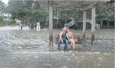  ?? /AFP ?? Keep on smiling: Brandon James and Brittany LaCombe sit on a swing surrounded by flood water from Lake Pontchartr­ain after Mandeville, Louisiana, was flooded on Saturday as hurricane Barry pounded the US state.