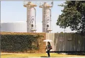  ?? Christina House Los Angeles Times ?? A WOMAN passes a Warren facility in Wilmington in June. L.A. faces two lawsuits from five oil entities.