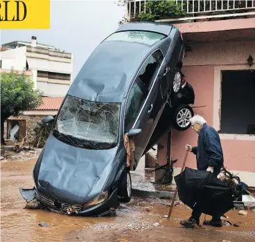  ?? PETROS GIANNAKOUR­IS / THE ASSOCIATED PRESS ?? A man walks past two cars pushed onto a house by the force of flood water in Mandra, western Athens, on Thursday. Rescue crews are searching for four people reported missing in the area following destructiv­e flash flooding.