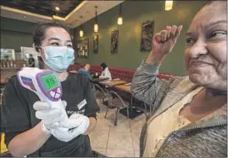  ?? MEL MELCON Los Angeles Times ?? GRACE MAGALLON, 63, right, here getting her temperatur­e taken at an Alhambra restaurant, says she’s “not really that concerned” about COVID-19.