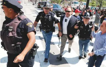  ?? AP ?? Conspiracy theorist Alex Jones is escorted by police out of a crowd of protesters outside the Republican convention in Cleveland last month.