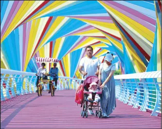  ?? AFP ?? People walk past a bridge adorned with rainbow-colored arches in Qingdao in China’s eastern Shandong province yesterday.