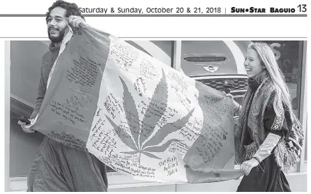  ?? AP Photo ?? People hold up a Canadian flag with a marijuana logo on it outside a government cannabis. Canada became the largest country with a legal national marijuana marketplac­e as sales began early Wednesday.