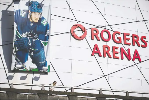  ?? — THE CANADIAN PRESS ?? A banner showing Canucks captain Bo Horvat overlooks a woman walking outside Rogers Arena. The province has made its pitch for Vancouver to be considered as a hub site, should the NHL decide to reopen its season with teams playing in the same city or cities.