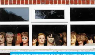  ?? — AFP ?? GORING, United Kingdom: Mannequins with wigs are pictured looking out of the window of a hairdresse­r’s salon, closed-down due to COVID-19, west of London on Saturday.