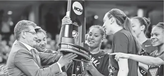  ?? JOHN DAVID MERCER/USA TODAY SPORTS ?? Geno Auriemma hands the 2015 women’s national championsh­ip trophy to forward Kaleena Mosqueda-Lewis as forward Breanna Stewart, right, looks on.