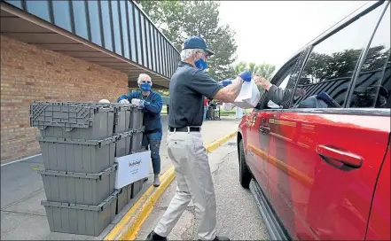  ?? JENNY SPARKS / Loveland Weekly ?? Kidspak volunteer Wil Brumley, center, hands food bags to a parent as Els Deininger, left, waits to get more bags out of a bin Friday in a drive-thru line outside Lincoln Elementary School in Loveland. Kidspak volunteers were distributi­ng food to students alongside the school district food program. Kidspak has seen a doubling of need during the pandemic.