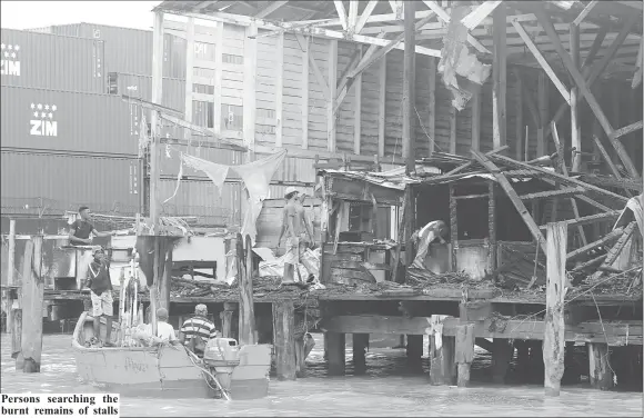  ??  ?? Persons searching the burnt remains of stalls at the Stabroek Market wharf (Photo by Terrence Thompson)