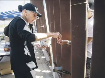  ?? Kate Morrissey For The Times ?? HUMANITARI­AN VOLUNTEER Maria Teresa Fernandez in San Diego offers cough drops to migrants stuck between the border walls. An official says too many are arriving for agents to clear the area quickly.