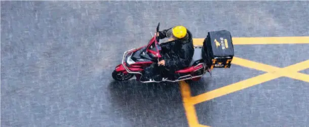  ??  ?? July 6, 2017, Beijing: A Meituan Waimai delivery worker braves the rain. Frequent thundersto­rms and sweltering summer heat in many Chinese cities inspire many to stay indoors instead of dining out. VCG