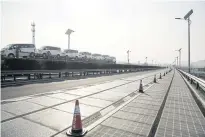  ??  ?? A car carrier drives past solar panels installed beneath transparen­t material in photovolta­ic lanes developed by Qilu Transporta­tion Developmen­t Group in Jinan, China. The panels inside generate enough electricit­y to power highway lights and 800 homes.
