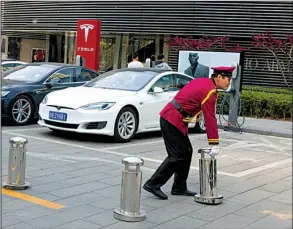  ?? AP/NG HAN GUAN ?? A security guard removes a barricade near a Tesla charging station earlier this month in Beijing. Tesla’s stock continues to rise as short sellers acquire shares, betting that the company will fail to meet its electric-car goals.