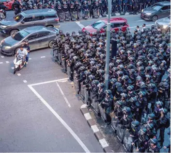  ?? — AFP ?? Motorists ride past riot police in Bangkok after Thailand issued an emergency decree following an anti-government rally the previous day.