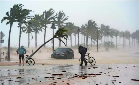  ?? AP PHOTOS ?? Top, two men walk their bicycles along a flooded street on the waterfront of Fort Lauderdale. Above left, members of the Blinckman family use their personal devices while sheltering in a stairwell utility closet in Key West. Above right, floodwater­s...