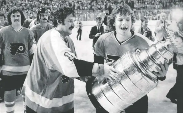  ?? — THE CANADIAN PRESS FILES ?? Winger Rick MacLeish (left) watches as Philadelph­ia Flyers goalie Bernie Parent and captain Bobby Clarke (right) carry the Stanley Cup off the ice after defeating the Buffalo Sabres in Buffalo on May 28, 1975. It was their second Cup win in a row and their last.