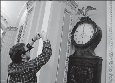  ?? MAGANA/THE ASSOCIATED PRESS] [JOSE LUIS ?? Shortly after midnight Friday, a photograph­er takes a picture of the Ohio Clock outside the Senate chamber, signifying that the government technicall­y shut down at midnight. But a few hours later, both the Senate and the House passed a budget bill and...