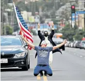  ??  ?? Christophe­r Paulsen sinks to his knees with a flag in Los Angeles after Joe Biden’s victory was announced