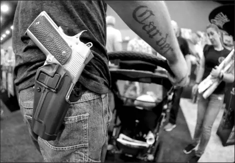  ?? MARK HUMPHREY / ASSOCIATED PRESS FILE (2016) ?? A man wears his handgun in a holster as he pushes his son in a stroller at the National Rif le Associatio­n convention May 21, 2016, in Louisville, Ky. Attendees at the convention are permitted to carry firearms under Kentucky’s open carry law.