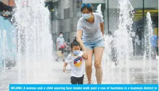  ?? — AFP ?? BEIJING: A woman and a child wearing face masks walk past a row of fountains in a business district in Beijing. China reported another 17 cases of the coronaviru­s, of which 14 were local cases in Beijing.