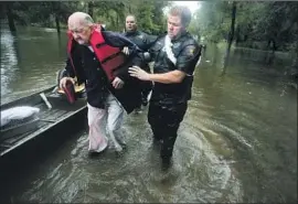  ?? Brett Coomer Houston Chronicle ?? POLICE OFFICER Mike Jones helps Fred Stewart to high ground Thursday after Stewart was rescued from his flooded neighborho­od in Splendora, Texas.